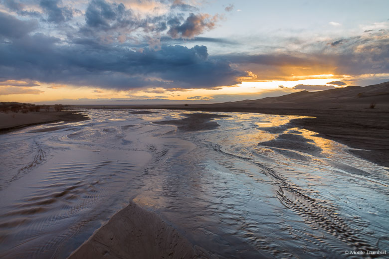 Medano Creek flows past the Great Sand Dunes towards the San Luis Valley at sunset in southern Colorado.