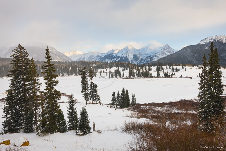 Sunlight streams through breaking snowstorm clouds and lights up the Grenadier Mountains beyond Molas Lake outside of Silverton, Colorado.